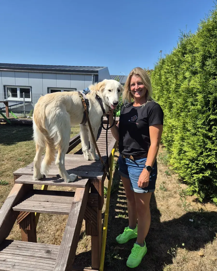 Meike Morschel steht lächelnd neben zwei Hunden auf einem Trainingspodest